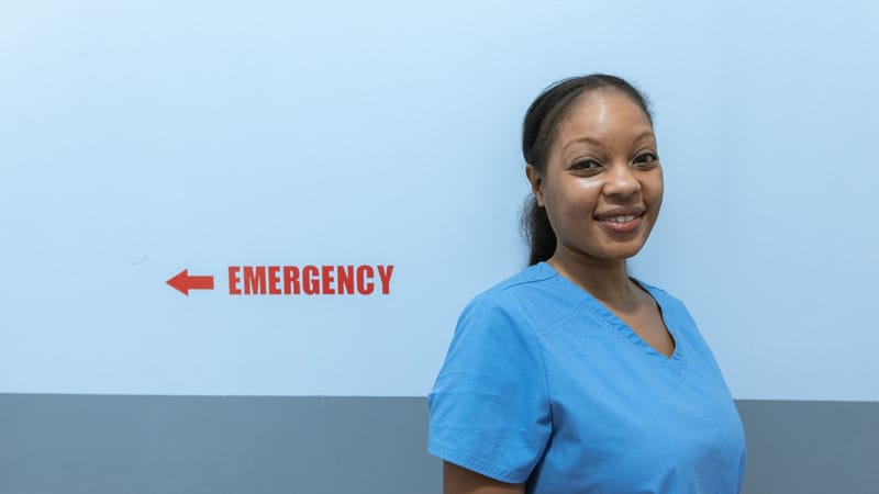 Travailleuse de la santé heureuse en tenue de soin se tenant près du panneau de salle d'urgence.