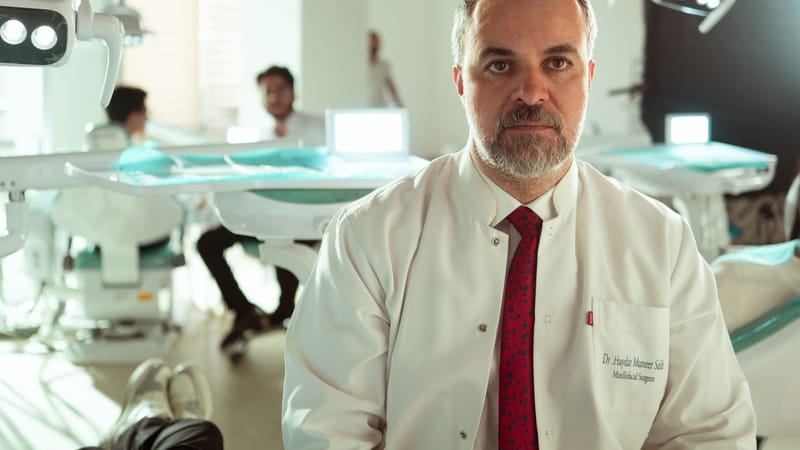 Un dentiste en blouse blanche est assis dans une clinique dentaire moderne, entouré d'équipements et d'assistants.