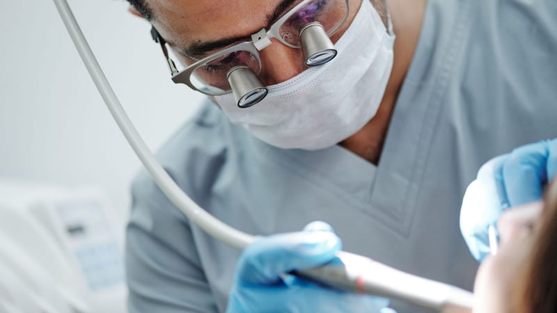 Dentiste portant des lunettes grossissantes réalisant une intervention dentaire dans une clinique.