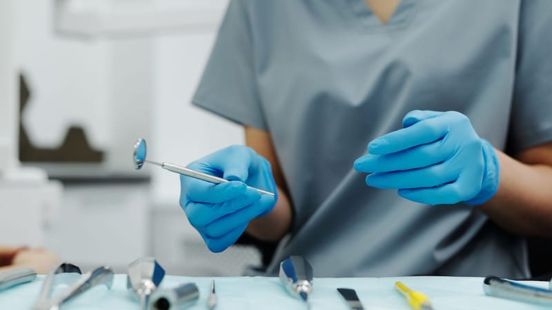 Les mains gantées du dentiste tenant des outils dentaires pendant une procédure. Focus sur l'hygiène et la précision.