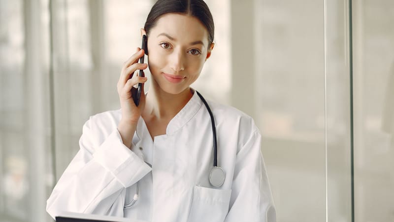 Médecin femme professionnelle en blouse blanche parlant au téléphone dans une clinique médicale.