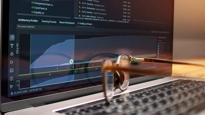 Écran d'ordinateur affichant du code et des graphiques de performance avec des lunettes reposant sur le clavier.