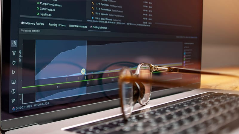 Écran d'ordinateur affichant du code et des graphiques de performance avec des lunettes reposant sur le clavier.