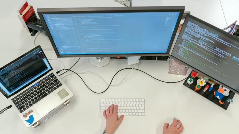 Une ingénieure logicielle féminine codant sur des double écrans et un ordinateur portable dans un bureau.