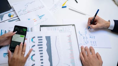 Des collègues collaborant sur des graphiques et des tableaux financiers en utilisant des documents mobiles et sur papier dans le bureau.