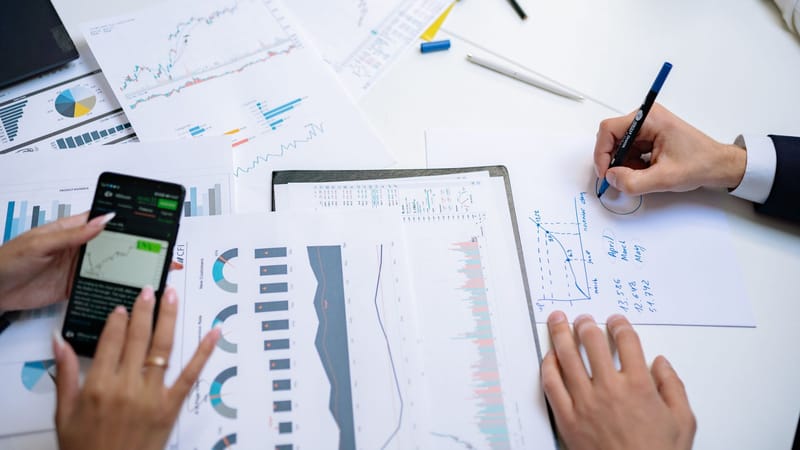 Des collègues collaborant sur des graphiques et des tableaux financiers en utilisant des documents mobiles et sur papier dans le bureau.
