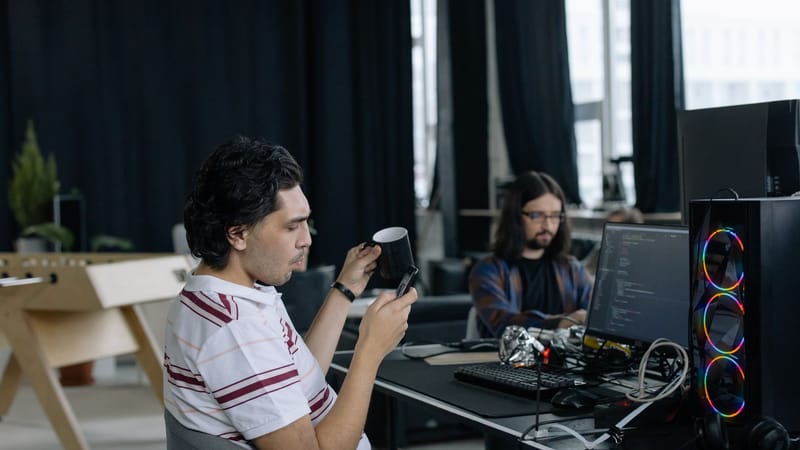 Deux programmeurs au travail dans un bureau moderne, concentrés sur le codage et profitant d'une pause café.
