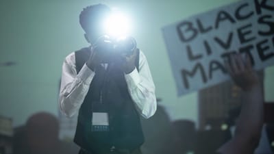 Un photojournaliste utilisant le flash de son appareil photo lors d'une manifestation avec un panneau Black Lives Matter.