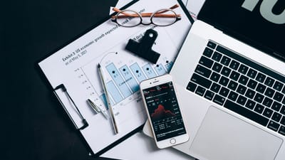 Vue de dessus de documents financiers, d'un ordinateur portable et d'un smartphone affichant des données boursières.