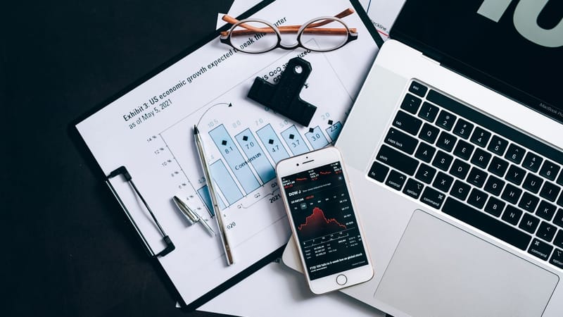 Vue de dessus de documents financiers, d'un ordinateur portable et d'un smartphone affichant des données boursières.