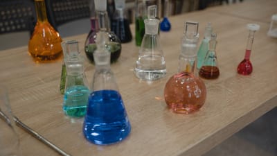 Flacons de laboratoire colorés avec divers liquides sur un bureau en bois pour des expériences scientifiques.