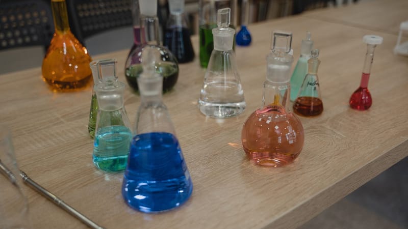 Flacons de laboratoire colorés avec divers liquides sur un bureau en bois pour des expériences scientifiques.