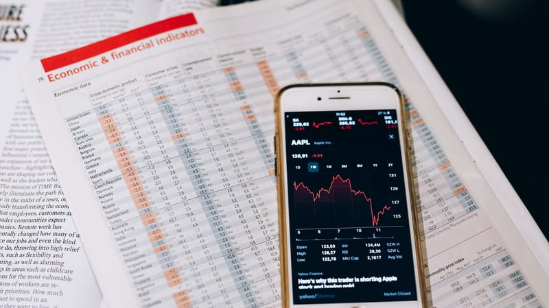 Smartphone affichant des données boursières sur des documents avec des graphiques financiers.