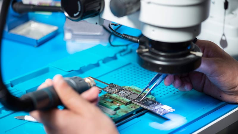 Gros plan d'un technicien réparant un circuit électronique sous un microscope dans un laboratoire à Toronto.