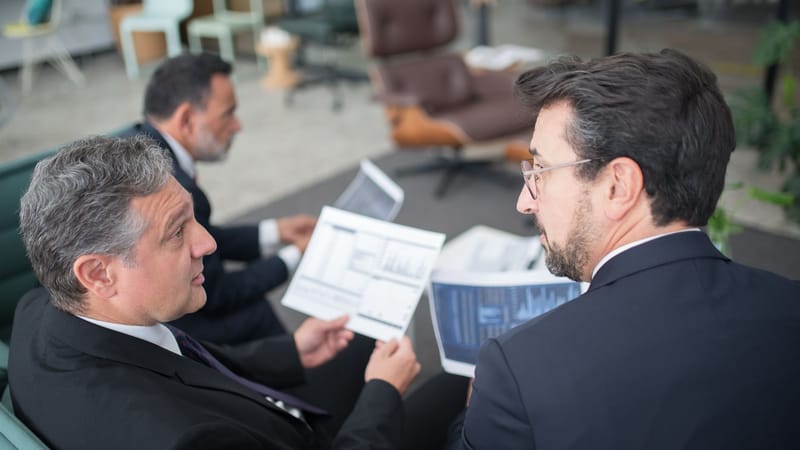 Trois hommes d'affaires discutent de documents financiers dans un cadre de bureau moderne.
