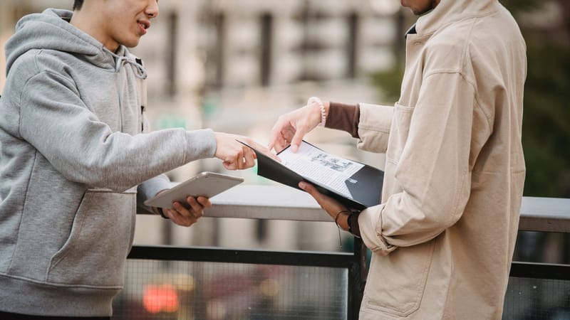 Deux jeunes adultes discutant d'un document à l'extérieur, utilisant une tablette. Concept de collaboration urbaine.