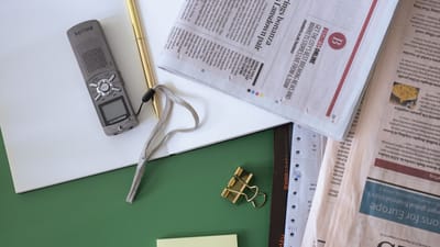Vue de dessus d'un bureau d'office avec des journaux, un bloc-notes et un dictafone sur une surface verte.