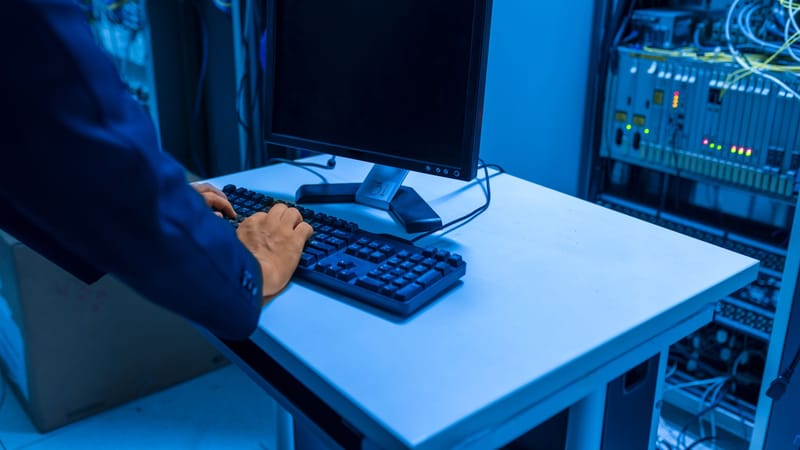 Un professionnel de l'informatique utilise un ordinateur dans une salle de serveurs, gérant des systèmes réseau et des appareils connectés.