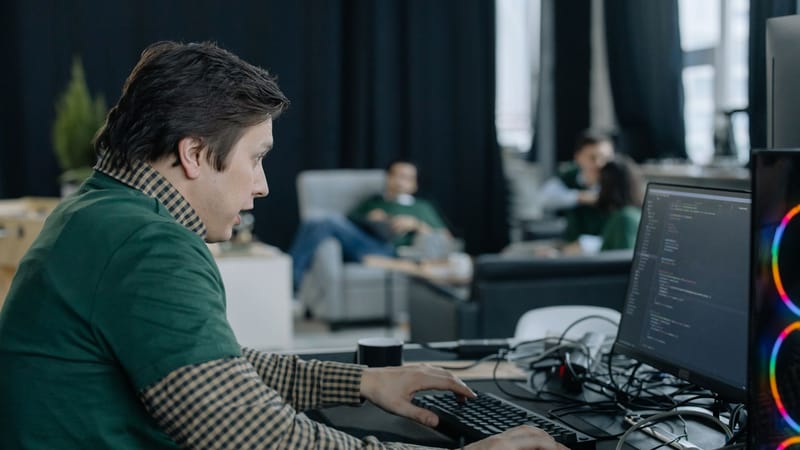 Programmeur masculin se concentrant sur le codage à l'ordinateur dans un environnement de bureau contemporain.