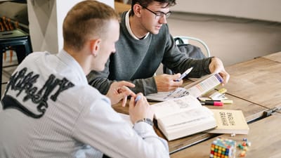 Deux jeunes hommes étudiant ensemble, concentrés sur des livres de grammaire anglaise dans un cadre intérieur moderne.