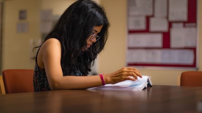 Jeune femme concentrée lisant un manuel à un bureau de bibliothèque universitaire à New Delhi.