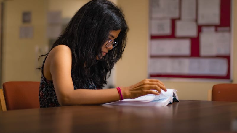Jeune femme concentrée lisant un manuel à un bureau de bibliothèque universitaire à New Delhi.