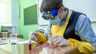 Étudiant en tenue de laboratoire effectuant une expérience de chimie avec équipement de sécurité.