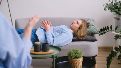 Homme participant à une séance de thérapie allongé sur un canapé gris confortable à l'intérieur.