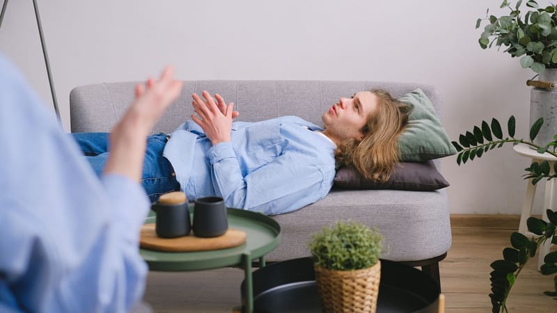Homme participant à une séance de thérapie allongé sur un canapé gris confortable à l'intérieur.