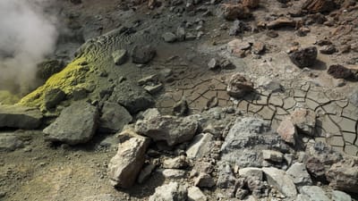 Vue dramatique d'une fumerolle de soufre avec un sol craqué et un terrain rocheux, exhalant de la vapeur géothermique.