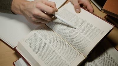Une main tenant un stylo tout en étudiant un livre ouvert, mettant en avant l'apprentissage et l'éducation.
