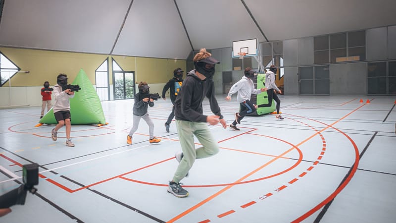 Des adolescents énergiques en action lors d'une partie de laser game en intérieur dans une salle de sport.