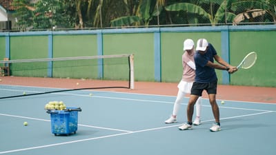 Un cours de tennis en cours, avec un entraîneur donnant des instructions à un joueur sur un court extérieur ensoleillé.