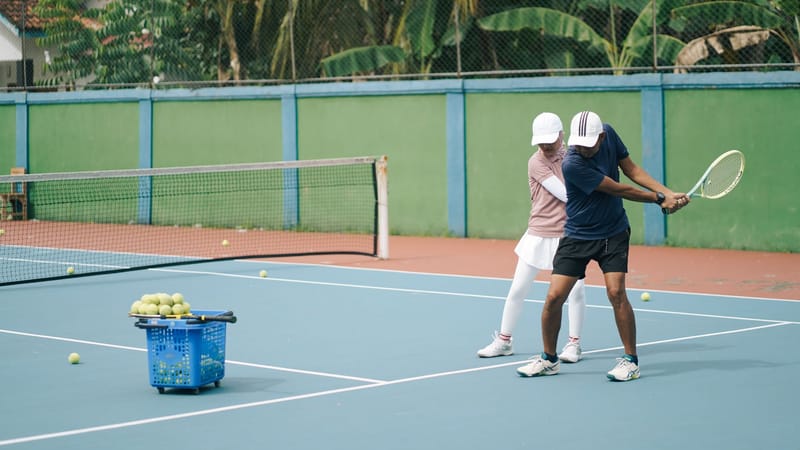 Un cours de tennis en cours, avec un entraîneur donnant des instructions à un joueur sur un court extérieur ensoleillé.
