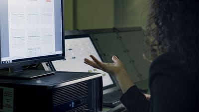 Une femme analyse des données sur un écran d'ordinateur dans un bureau moderne, se concentrant sur la recherche technologique.