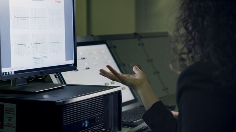 Une femme analyse des données sur un écran d'ordinateur dans un bureau moderne, se concentrant sur la recherche technologique.