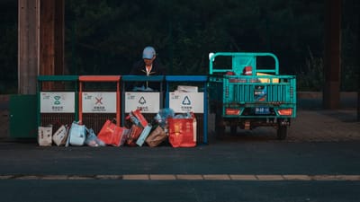Un employé range des déchets dans un centre de recyclage à côté d'un véhicule stationné, scène de soirée.