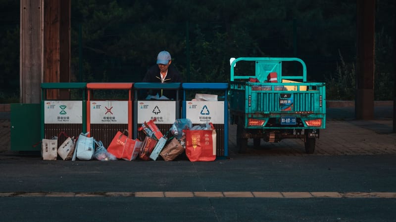 Un employé range des déchets dans un centre de recyclage à côté d'un véhicule stationné, scène de soirée.