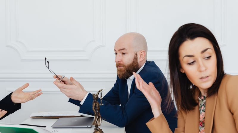 Trois adultes dans une discussion animée avec des documents légaux, à l'intérieur.