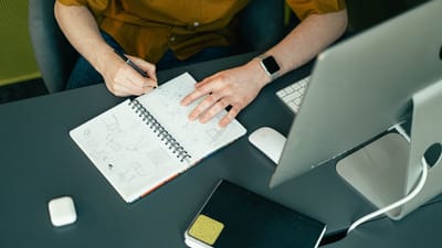 Une personne esquissant dans un carnet au bureau moderne avec un ordinateur et des accessoires.