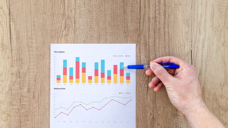 Une main pointe un stylo sur des graphiques d'affaires sur une table en bois, mettant en avant l'analyse des données.