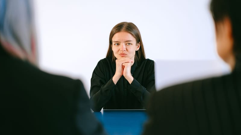 Une femme lors d'un entretien d'embauche face à deux personnes autour d'une table de bureau, se concentrant intensément.