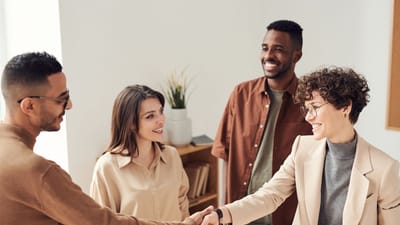 Quatre collègues souriants se serrant la main dans un bureau lumineux.