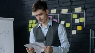Un jeune homme examinant des documents dans un bureau avec un mur en briques noires et un fond de notes autocollantes.