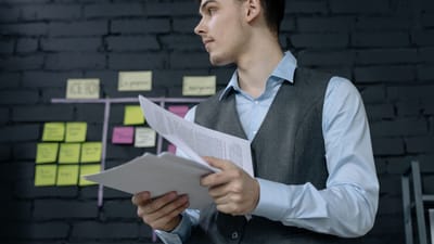 Jeune professionnel masculin analysant des documents de projet dans un cadre de bureau moderne avec un tableau de tâches.