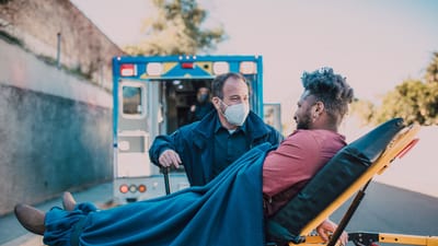 Un ambulancier aide un homme sur une civière près d'une ambulance en extérieur.