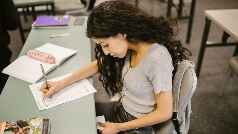 Jeune étudiant universitaire écrivant sur une feuille d'examen dans une salle de classe, concentré sur la réussite académique.