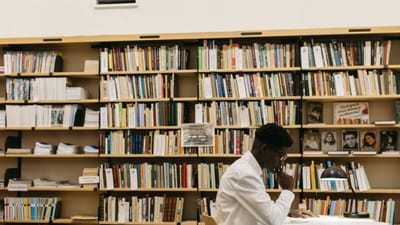Un homme étudiant avec attention dans une bibliothèque remplie d'étagères de livres, créant une atmosphère réfléchie.