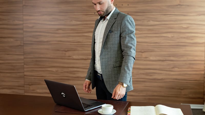 Homme d'affaires en blazer gris travaillant sur un ordinateur portable à son bureau.