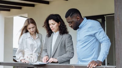 Trois adultes examinant des documents sur un balcon lors d'une consultation immobilière.